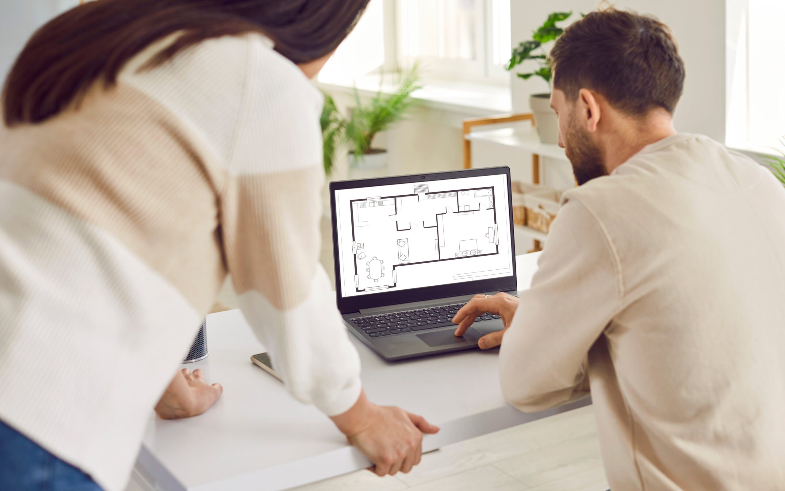 Two people looking at a laptop with plans on it.